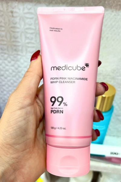 close up photo of hand holding product medicube pdrn pink niacinamide whip cleanser